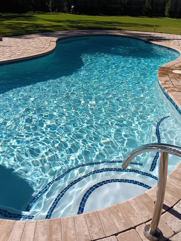 Turquoise backyard swimming pool with curved shape, brick patio deck, metal ladder, and manicured lawn in background