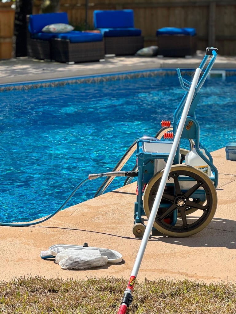 Wheelchair accessible pool lift positioned at the edge of a swimming pool with blue lounge chairs visible in the background