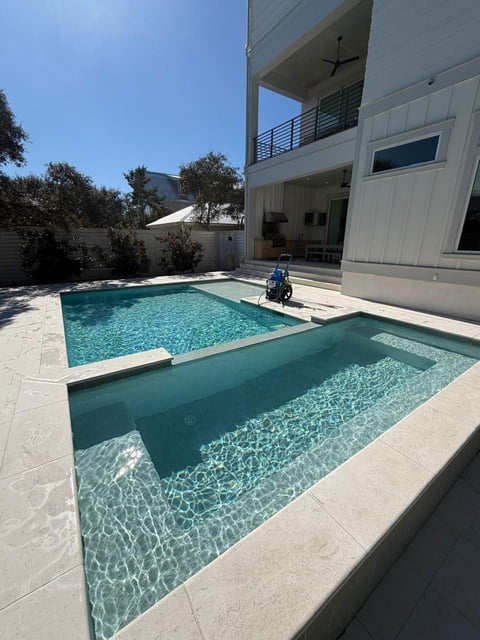 Modern two-story white house with two swimming pools and tan patio on a sunny day