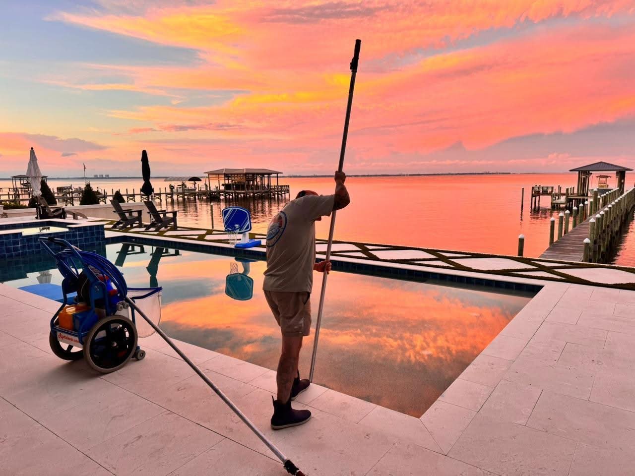 Man stretching on waterfront dock at sunrise with boats and pink sky reflected in calm water