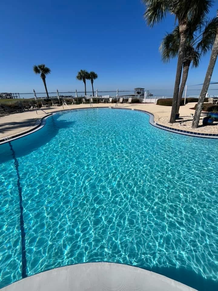 Curved resort pool with crystal clear turquoise water, palm trees, and sandy beach under blue sky